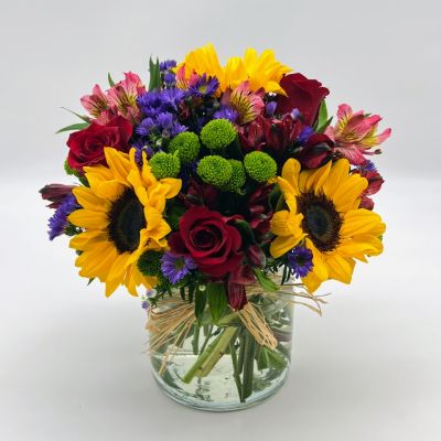 <p>Reminiscent of strolling through a field of flowers, this colorful arrangement captures features magnificent sunflowers, alstroemeria and poms set in a trendy mason jar with a natural raffia bow.</p>